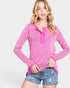 Woman wearing a pink long-sleeve top and denim shorts on a light gray background