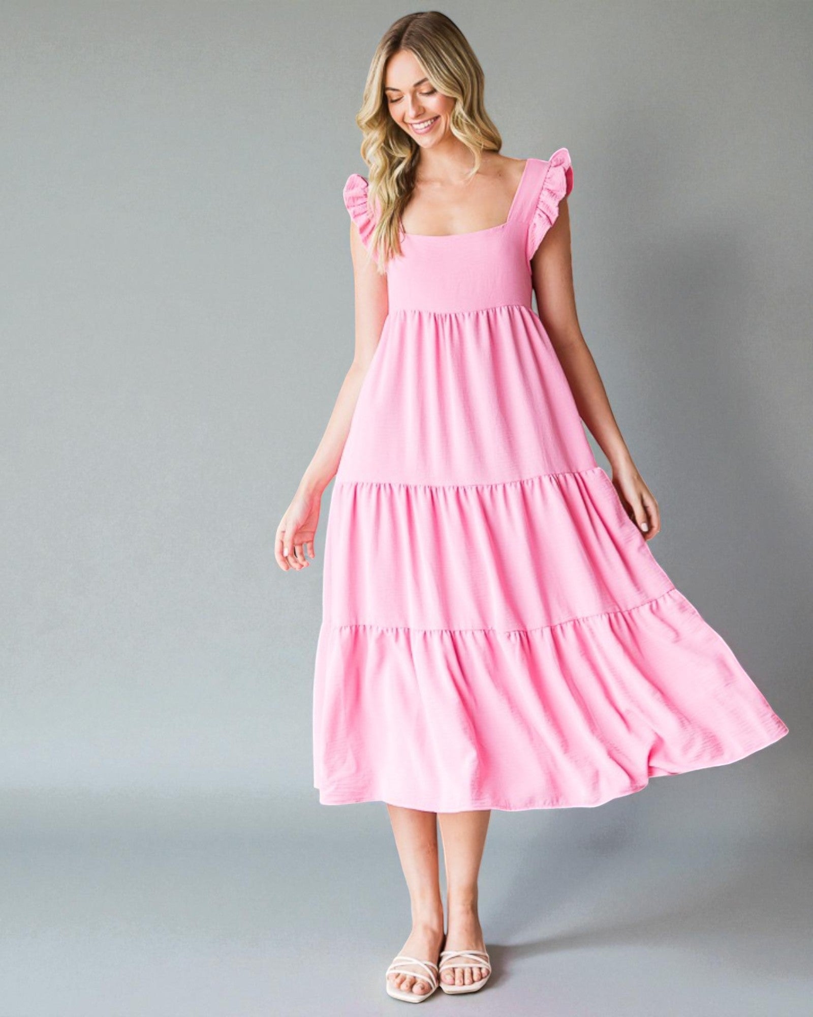 Woman wearing a pink dress with ruffled shoulders on a gray background