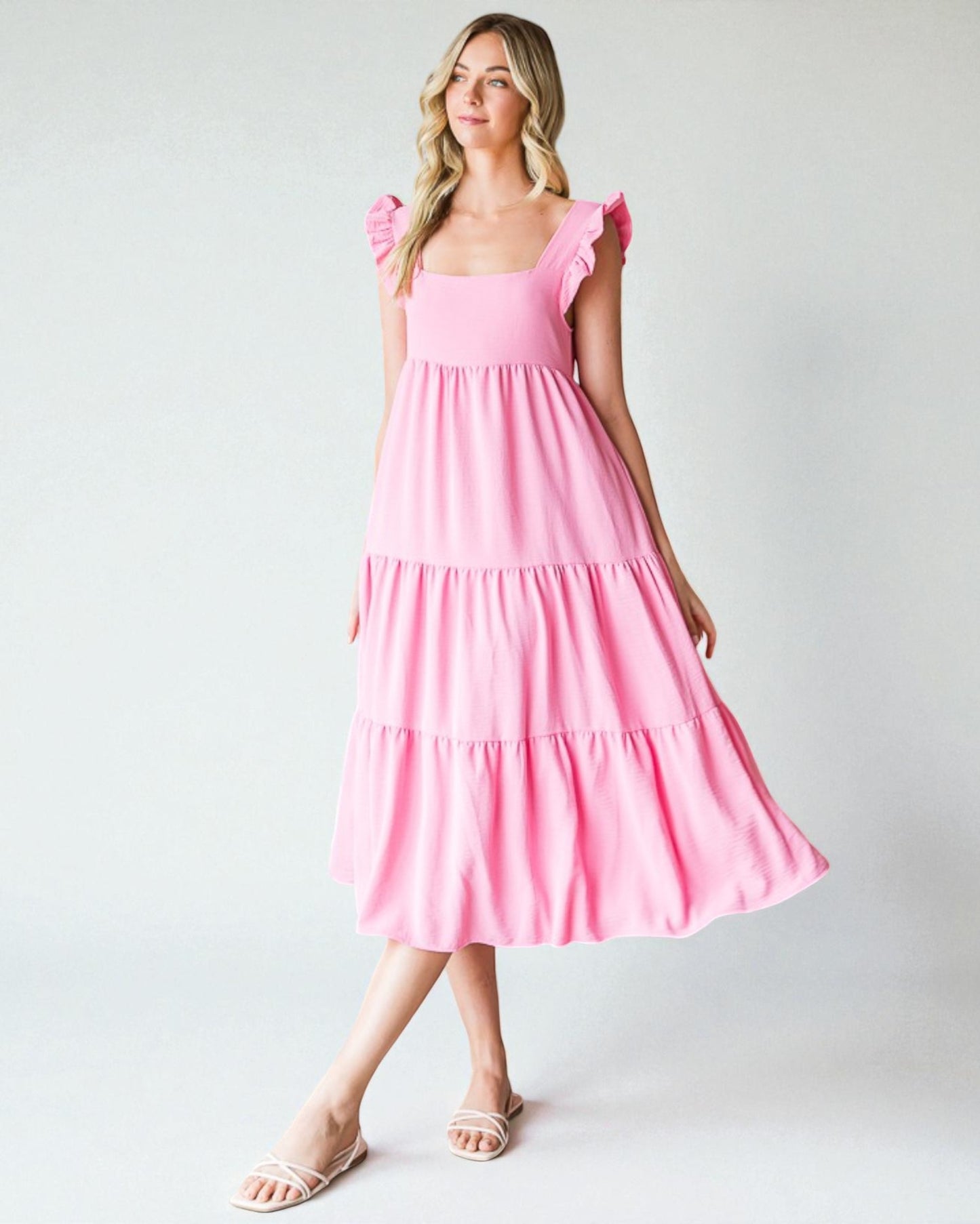 Woman wearing a pink dress with ruffled sleeves against a white background