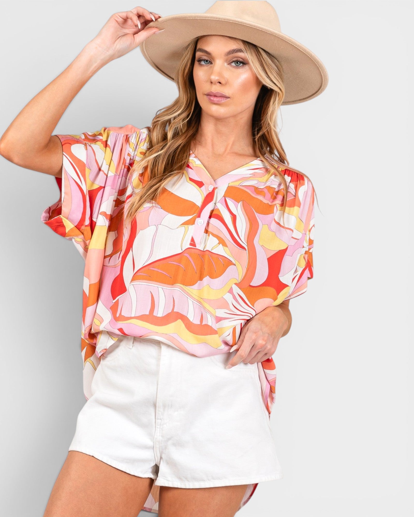 Woman wearing a colorful blouse and white shorts with a beige hat on a light gray background