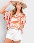 Woman wearing a colorful blouse and white shorts with a beige hat on a light gray background