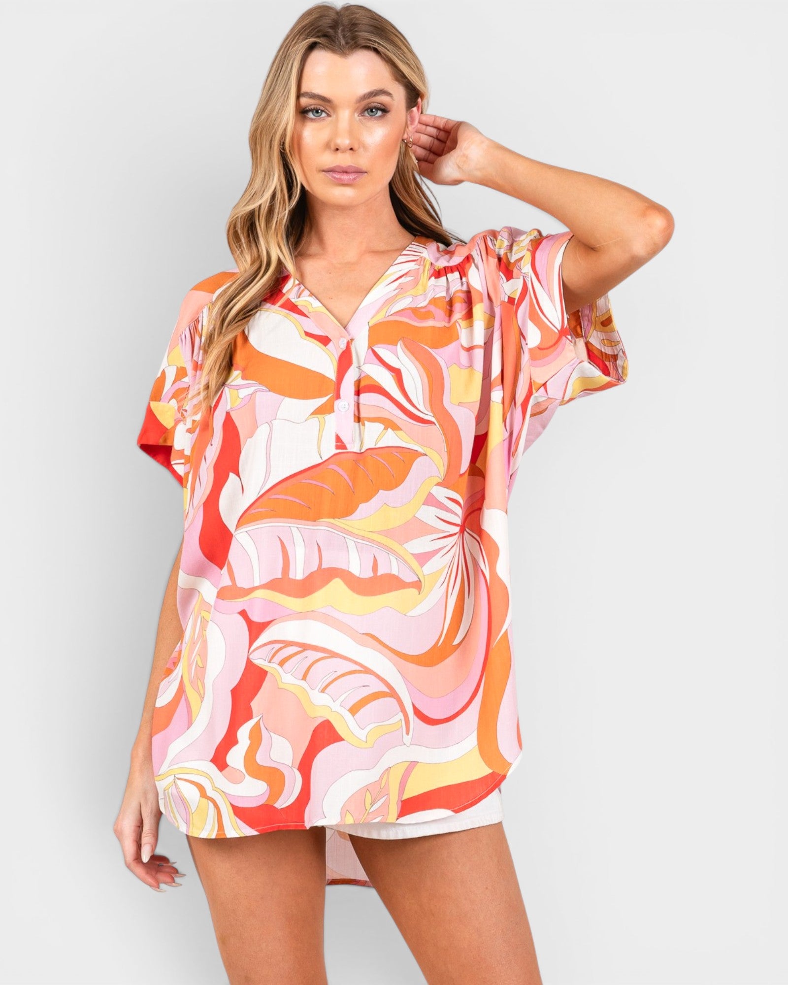 Woman wearing a colorful tropical print dress on a plain background