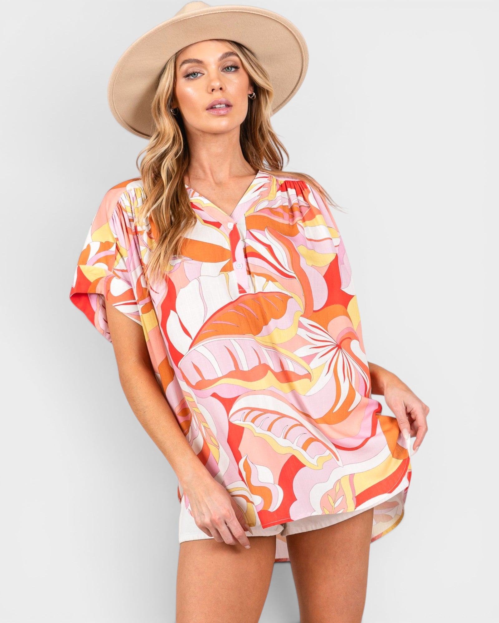 Woman wearing a colorful patterned cover-up dress and beige hat on a white background