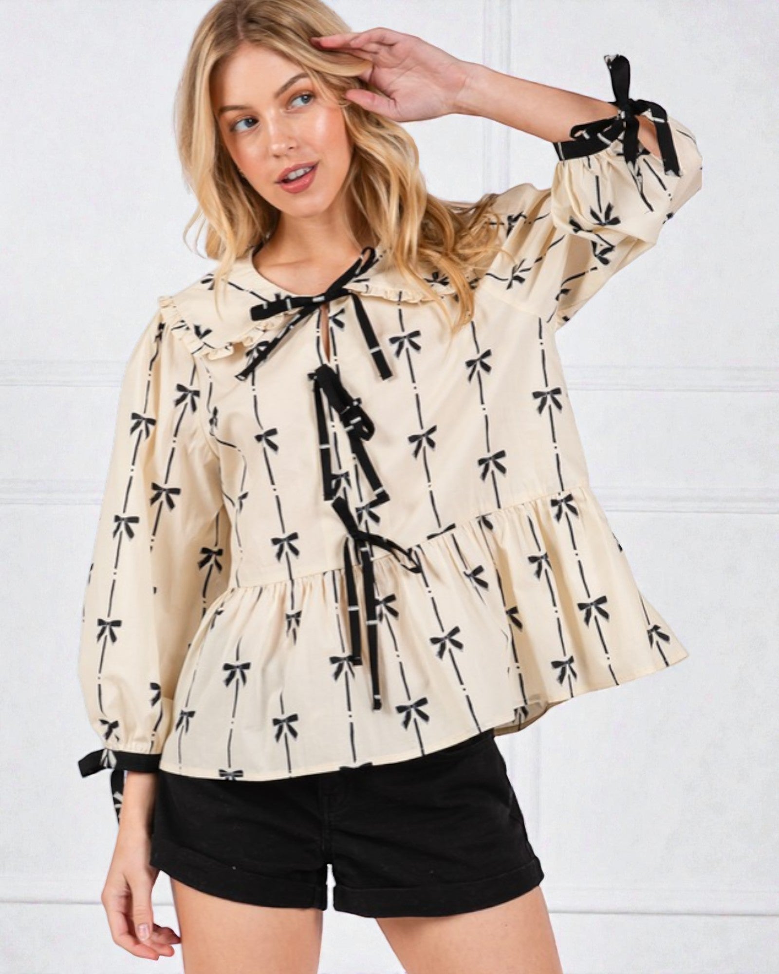 Woman wearing a beige blouse with black bow patterns against a white background