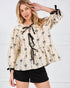 Woman wearing a beige blouse with black bow patterns against a white background