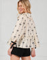 Woman wearing a beige blouse with black bow pattern and black shorts on a white background