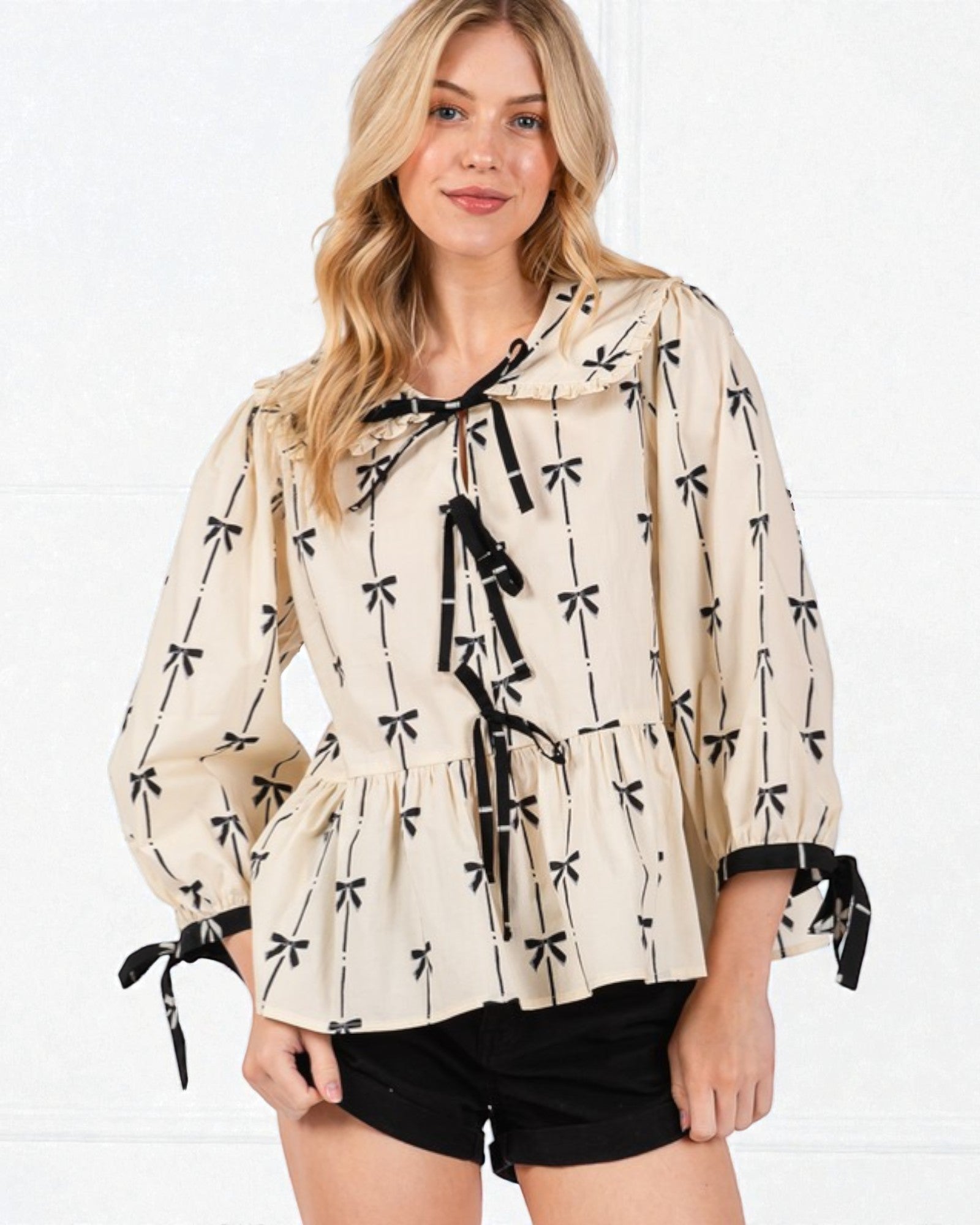 Woman wearing a beige blouse with black bow pattern on a white background