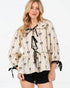 Woman wearing a beige blouse with black bow pattern on a white background
