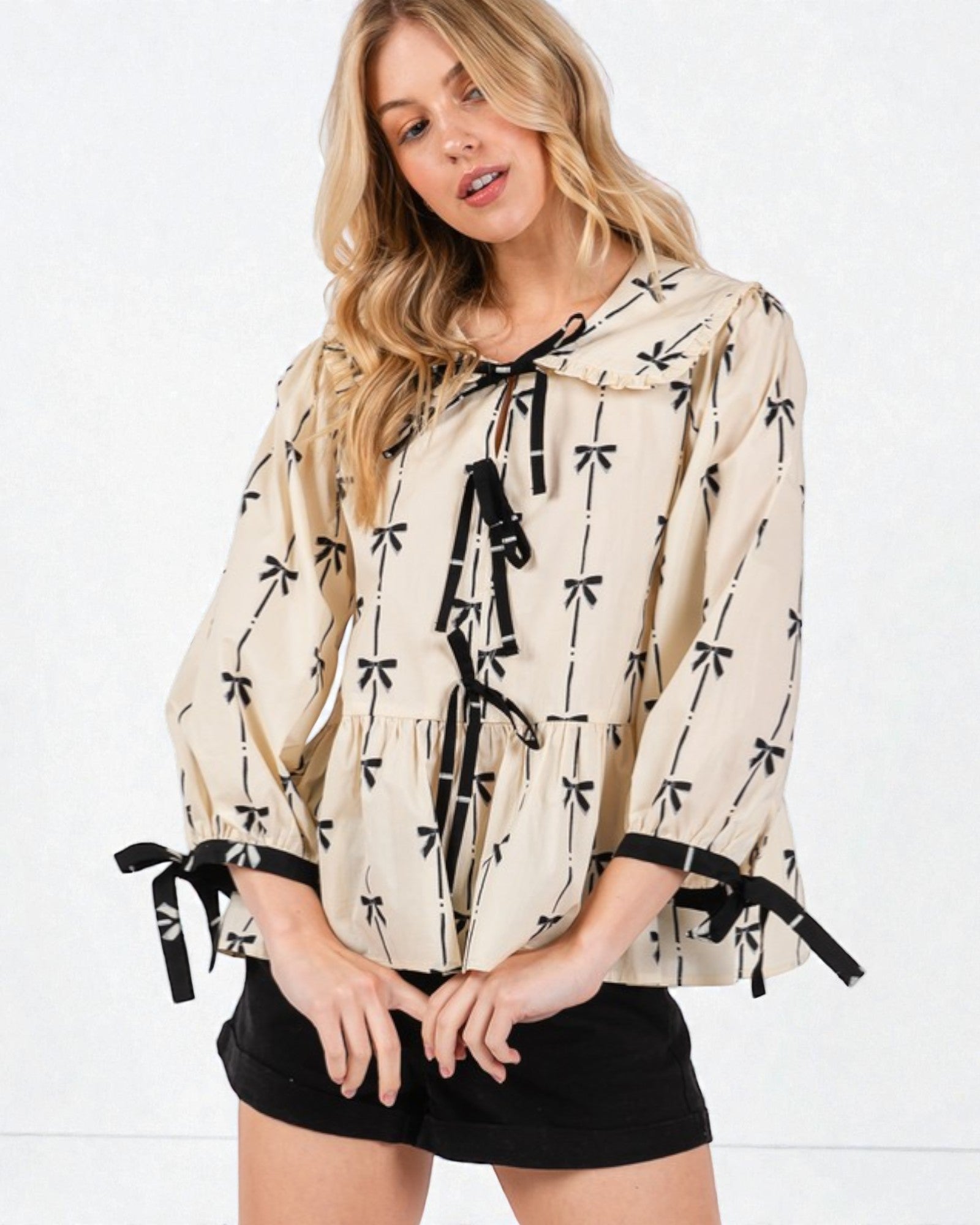 Woman wearing a beige blouse with black bow patterns on a white background