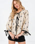 Woman wearing a beige blouse with black bow patterns on a white background