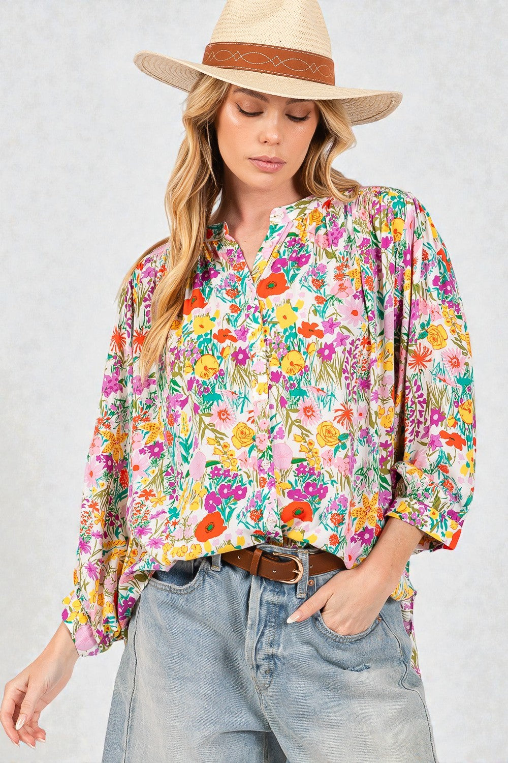 Woman wearing a colorful floral blouse and straw hat against a plain background