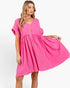 A woman modeling a bright pink short-sleeve dress with a button-front bodice and gathered skirt, photographed against a clean white studio background.