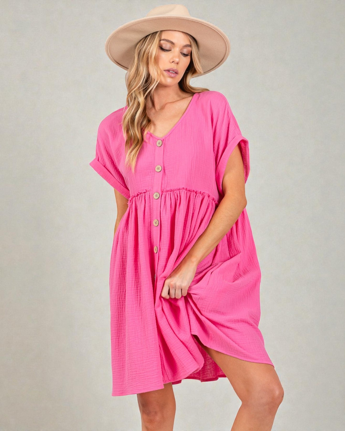 Woman wearing a pink dress with a beige hat on a gray background