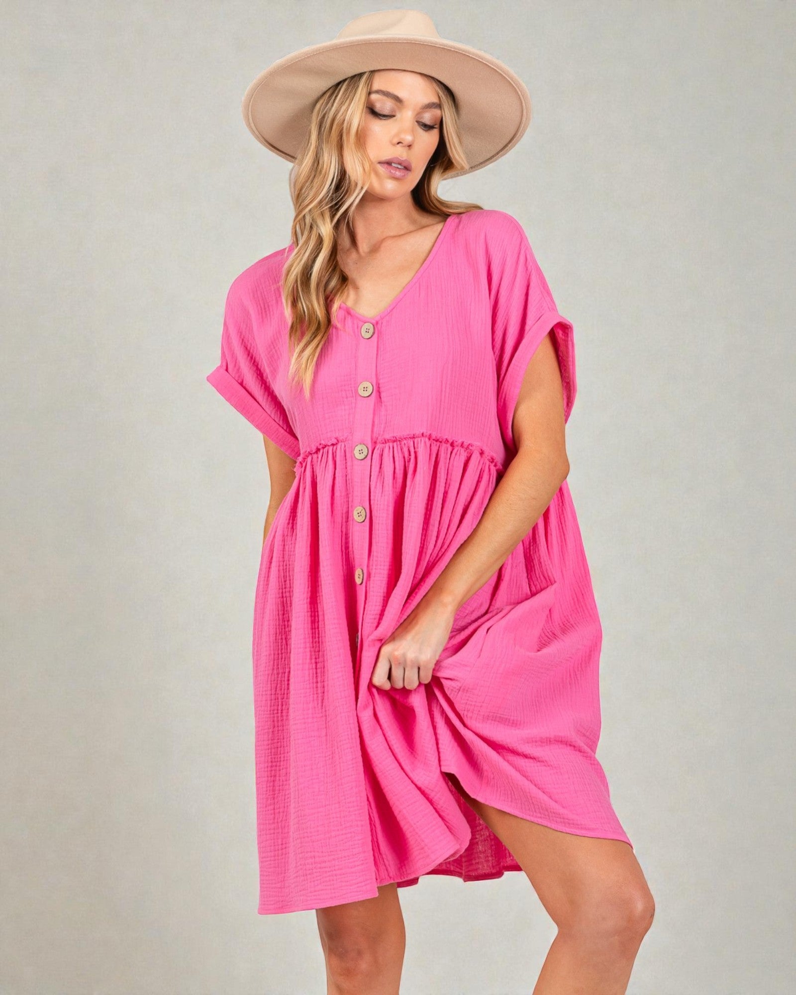 Woman wearing a pink dress with a beige hat on a gray background