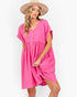 A woman wearing a bright pink short-sleeve button-front dress and a beige wide-brim hat, photographed against a plain light background.