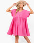 A woman wearing a bright pink short-sleeve babydoll dress with a button-down front and a beige wide-brim hat, posing against a plain white background.