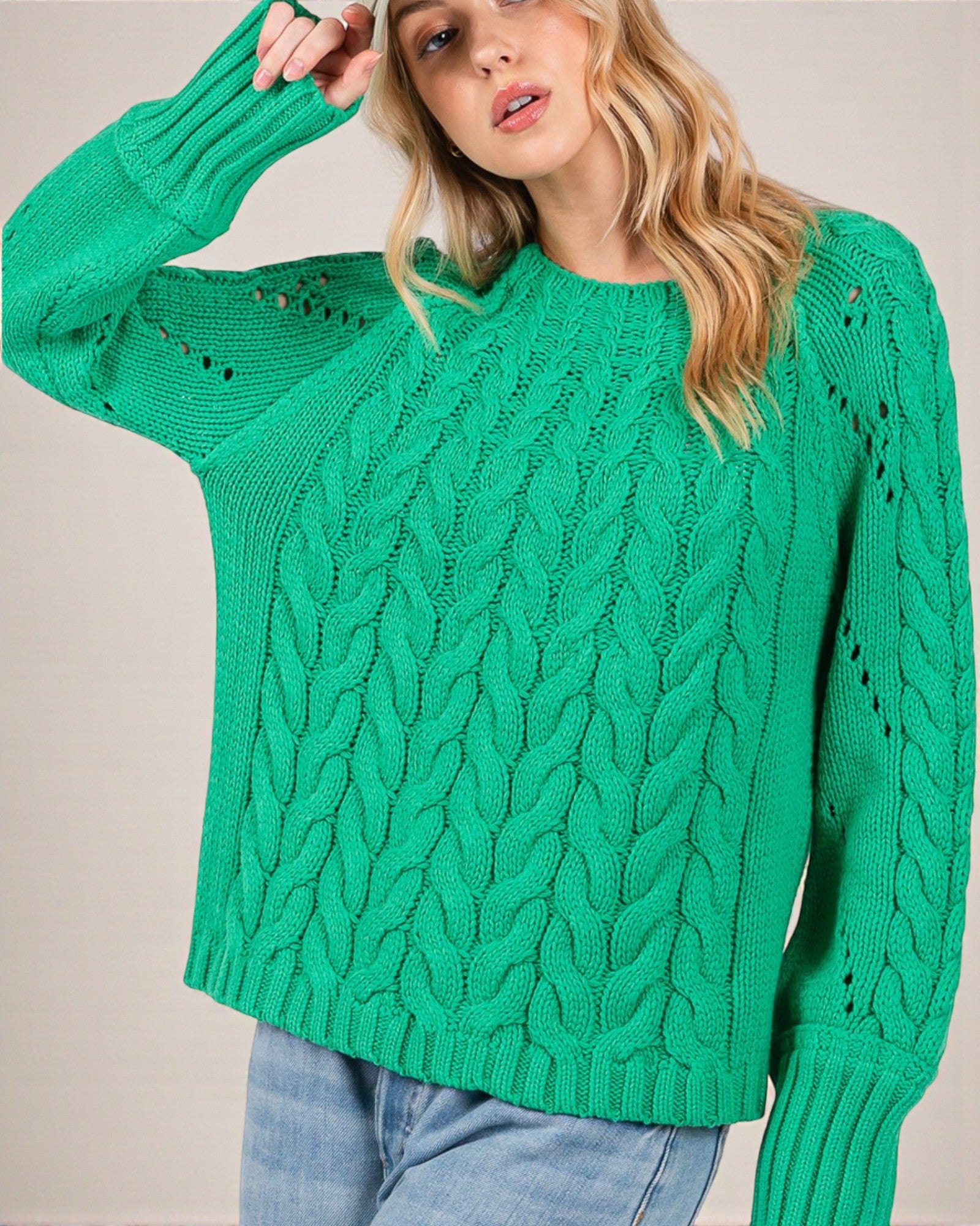 Woman wearing a green cable knit sweater against a plain background