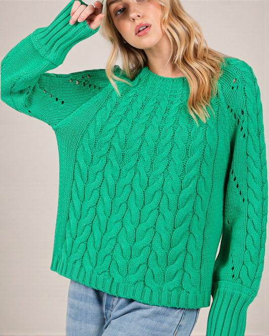 Woman wearing a green cable knit sweater against a plain background