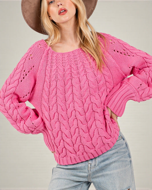 Woman wearing a pink knitted sweater and light blue jeans against a neutral background