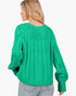 A woman shown from the back wearing a bright green cable-knit sweater and light gray jeans against a plain white background.