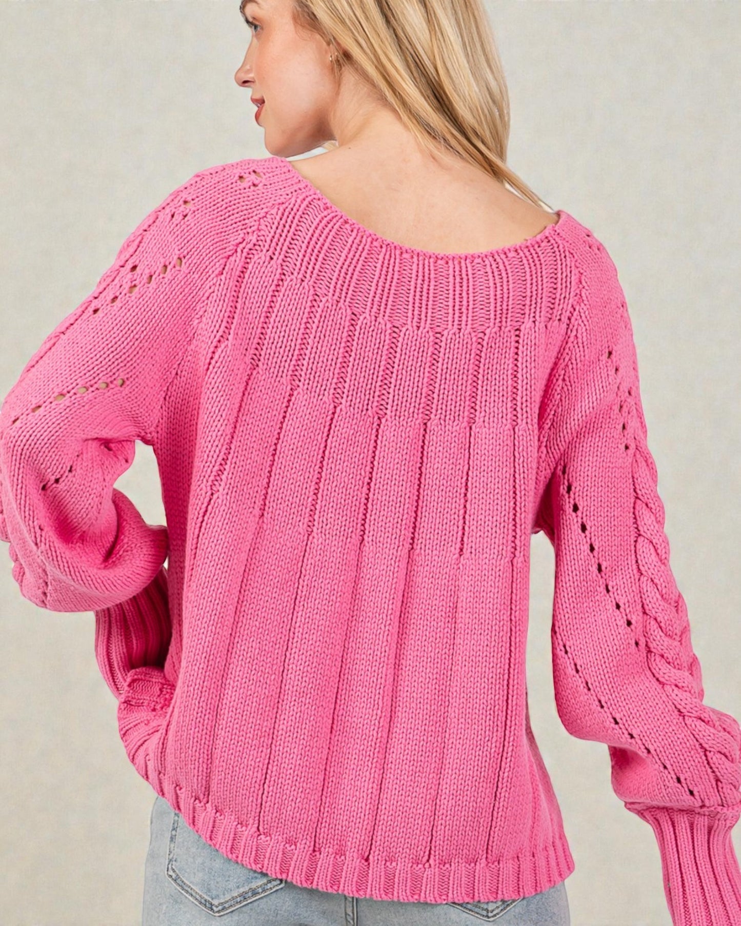 Person wearing a pink knitted sweater against a neutral background