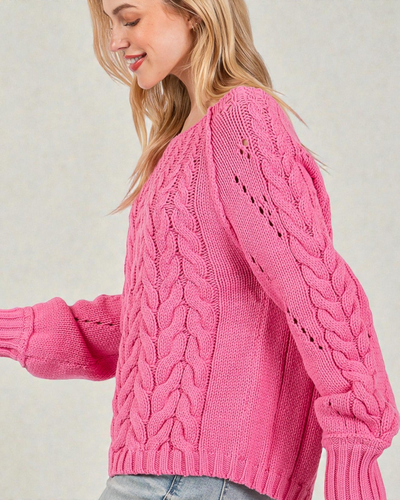 Person wearing a pink cable knit sweater against a light background