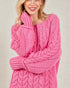 Woman wearing a pink cable knit sweater against a plain background