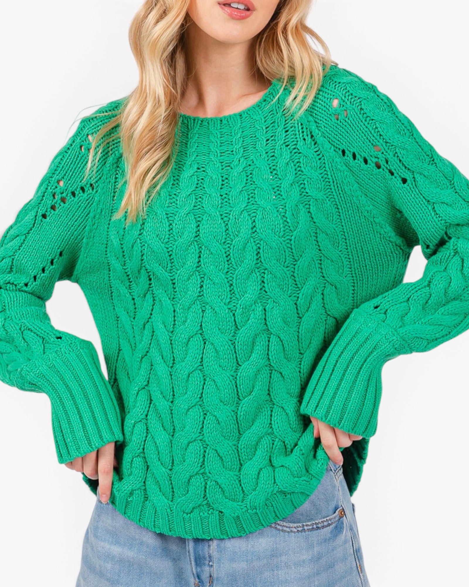 A woman wearing a bright green cable-knit sweater with distressed details on the shoulders and cuffs, paired with light blue jeans against a plain white background.