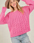 Woman wearing a pink cable knit sweater with a plain background