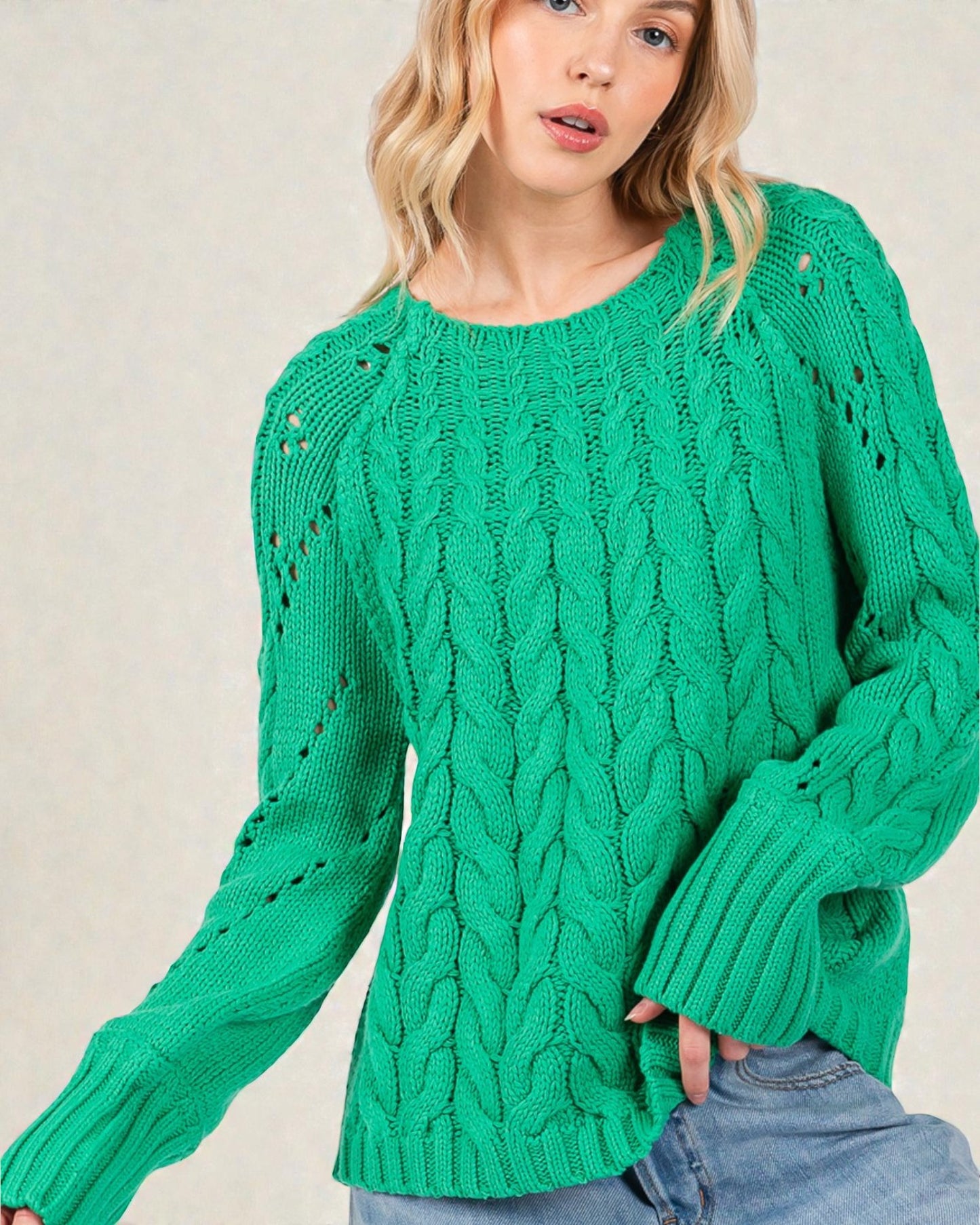 Woman wearing a green cable knit sweater against a plain background