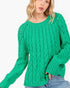 A woman wearing a bright green cable-knit sweater with textured knit details and wide sleeves, paired with blue jeans, against a plain white background.