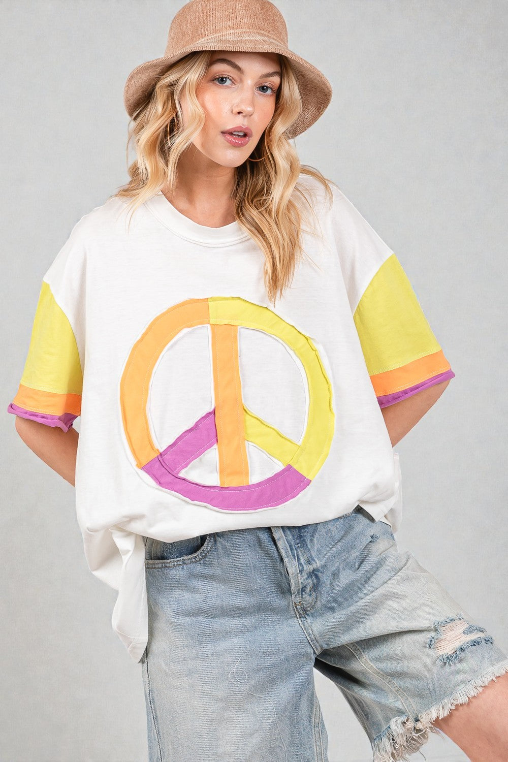 Person wearing a white t-shirt with a peace symbol design, colorful sleeves, and denim shorts on a gray background.