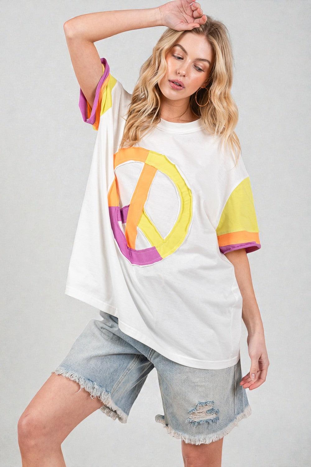 Woman wearing a white t-shirt with a colorful peace symbol design on a plain background