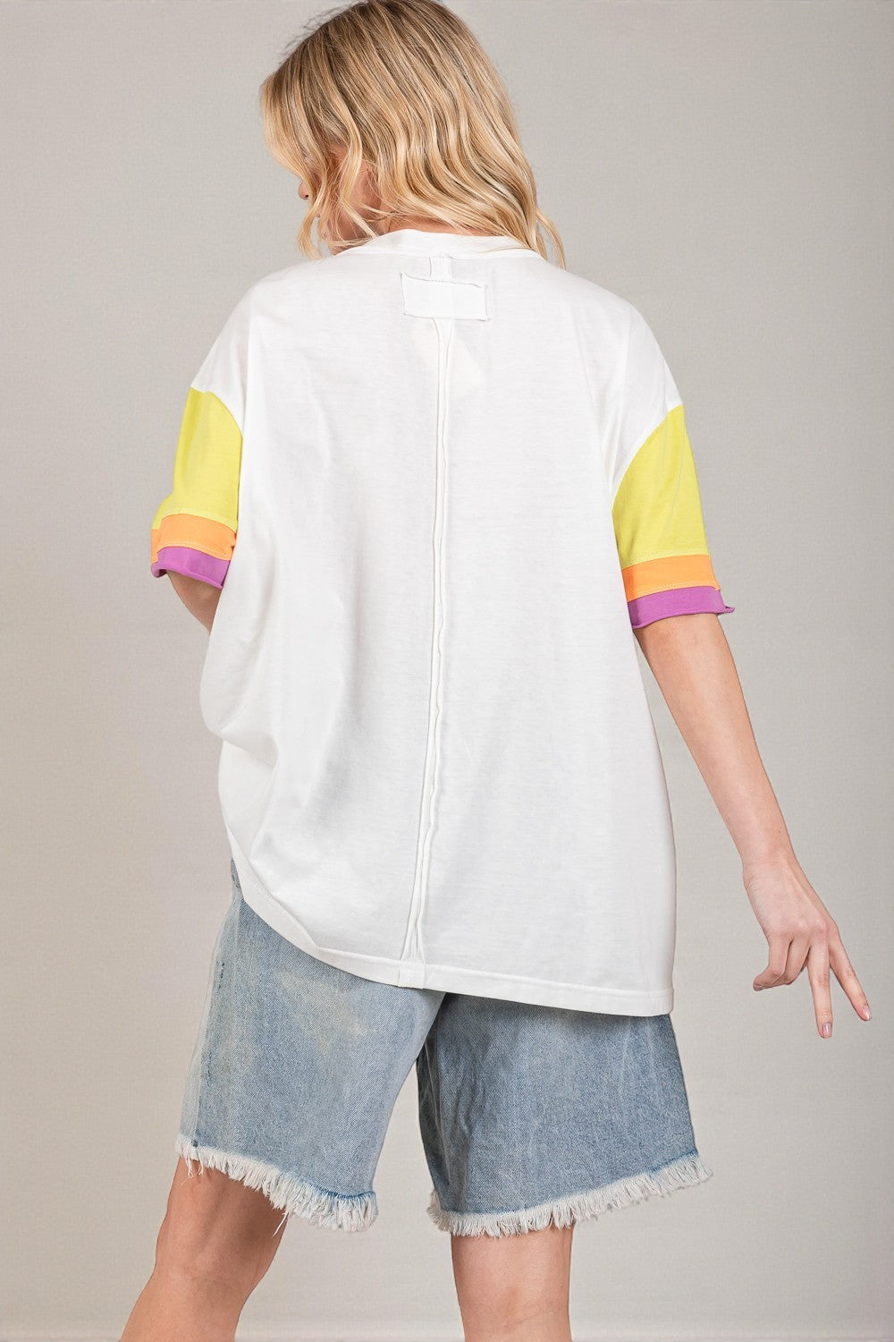 Person wearing a white shirt with colorful sleeves and denim shorts on a plain background