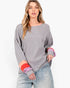A woman modeling a gray long-sleeve knit sweater with color-blocked cuffs in red, pink, and purple, paired with light-wash jeans against a plain white studio background.