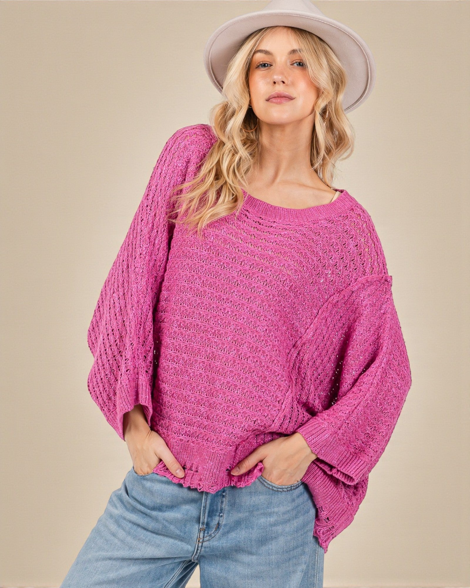 Woman wearing a pink sweater and light blue jeans against a beige background