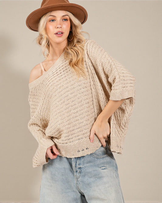 Woman wearing a beige knitted sweater and brown hat against a plain background