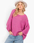A woman wearing a bright pink open-knit sweater with balloon sleeves, paired with light blue jeans and a beige wide-brim hat, against a plain white background.