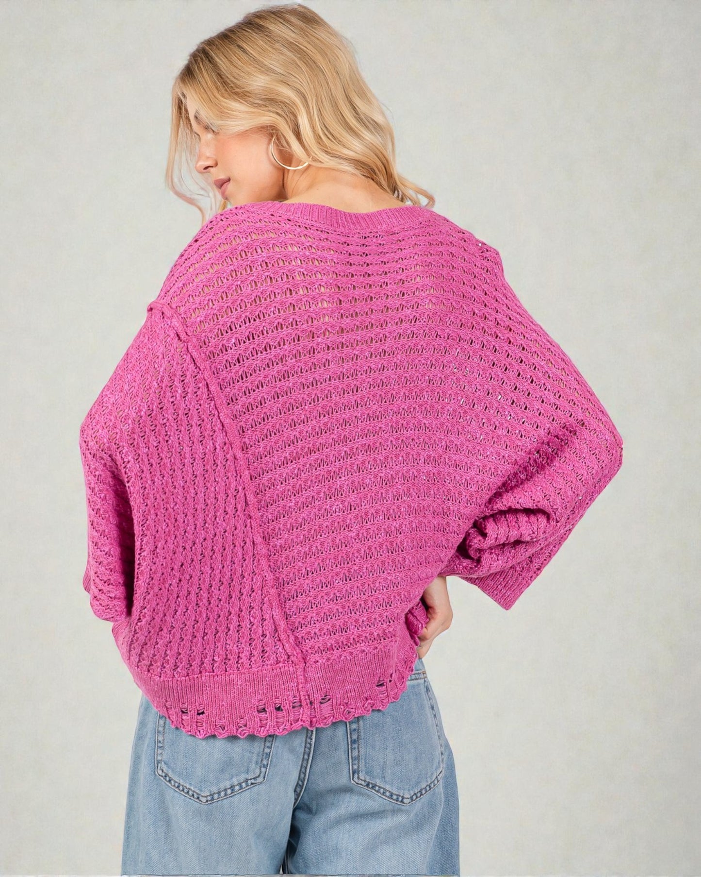 Woman wearing a pink knitted sweater and blue jeans on a plain background