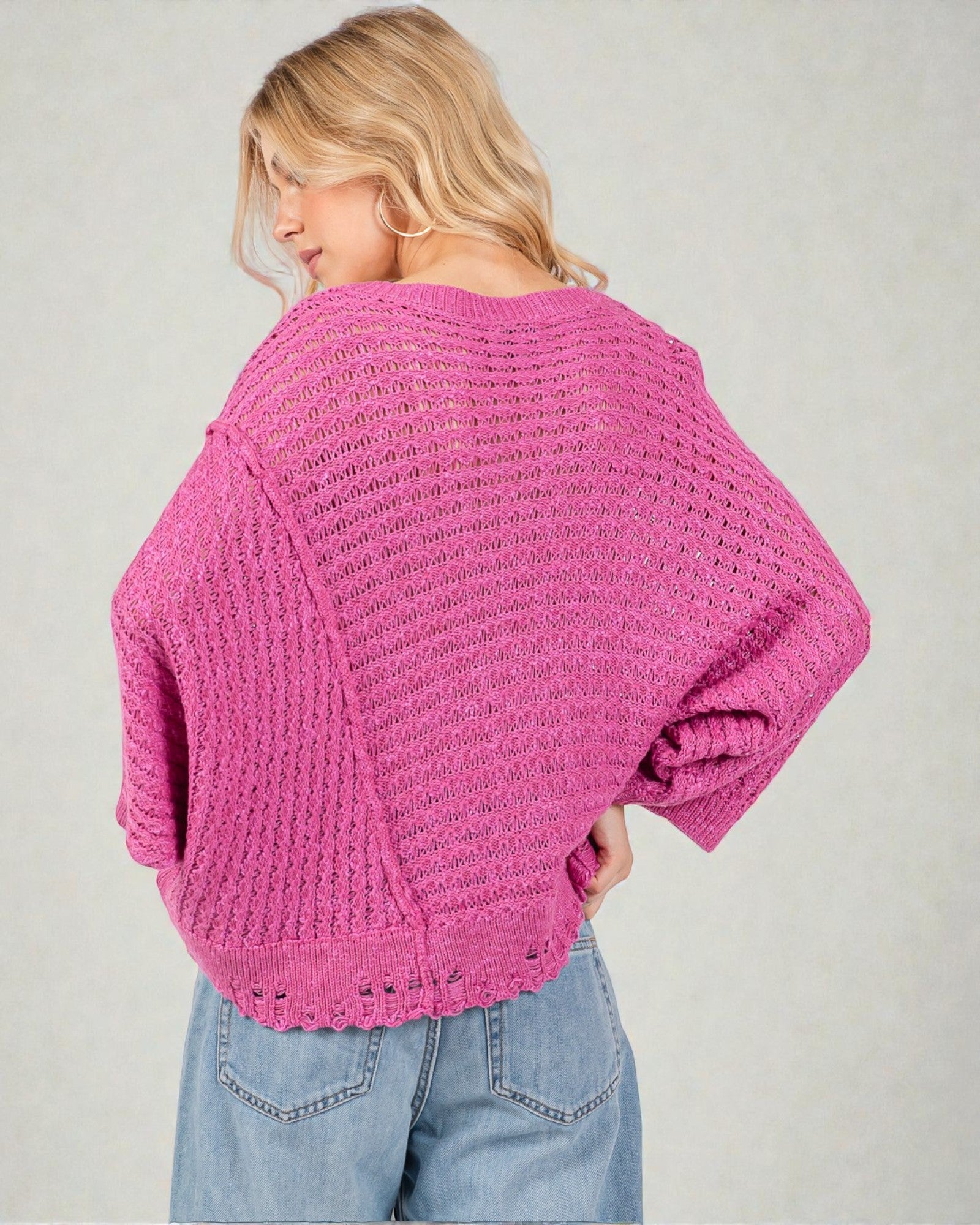 Woman wearing a pink knitted sweater and blue jeans on a plain background