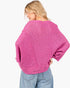 A woman shown from the back wearing a bright pink chunky knit sweater and light blue jeans against a plain white background.