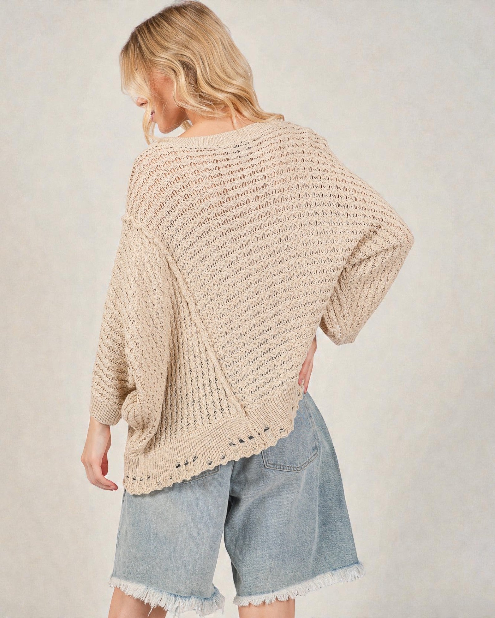 Woman wearing a beige knitted sweater and denim shorts on a plain background