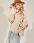 Woman wearing a beige knit sweater and brown hat against a plain background