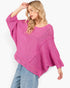 A woman wearing a bright pink open-knit sweater with wide batwing sleeves and light blue jeans, posed against a clean white background.