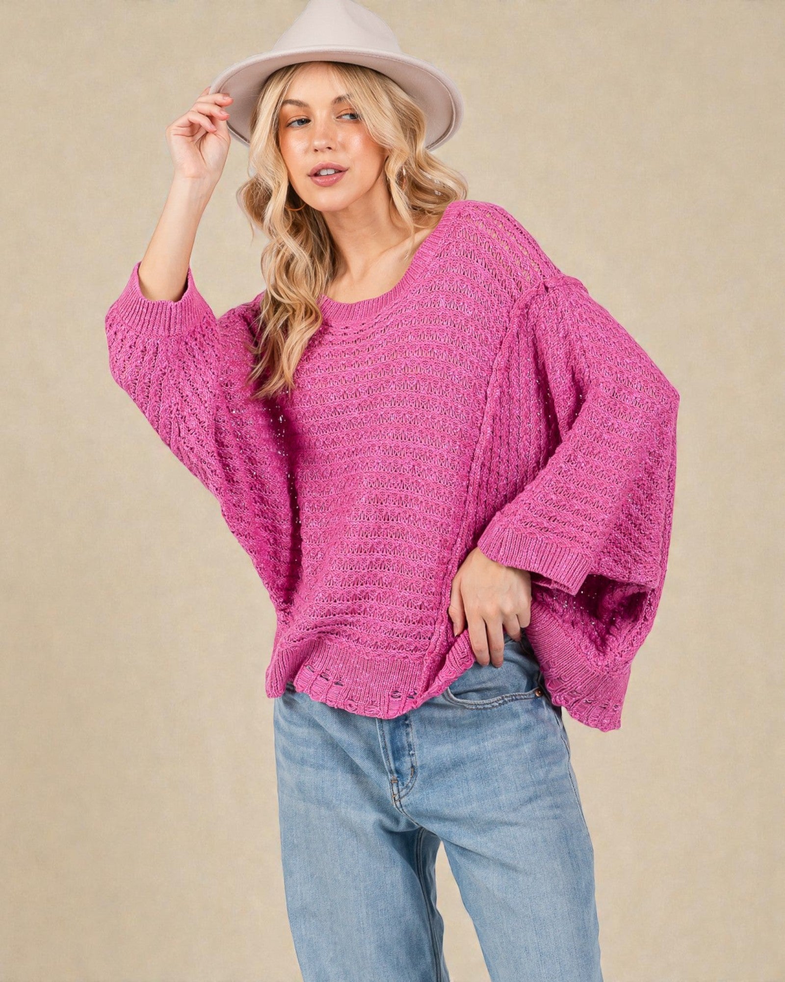 Woman wearing a pink sweater and light blue jeans against a beige background