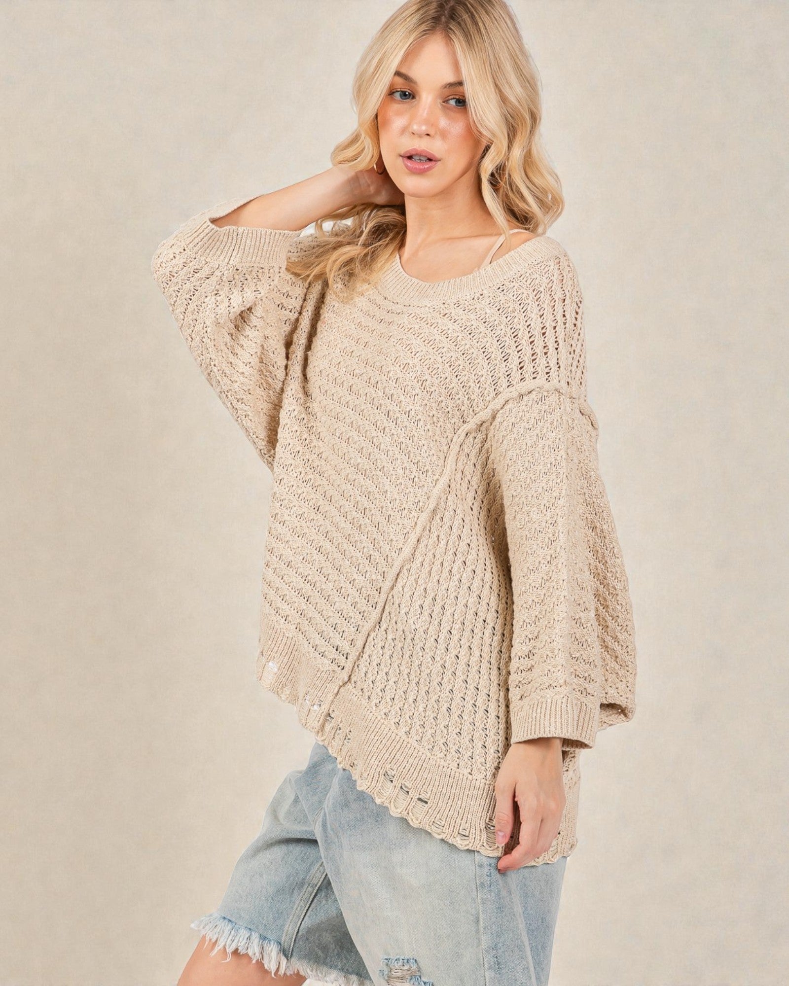 Woman wearing a beige knitted sweater and denim shorts on a plain background