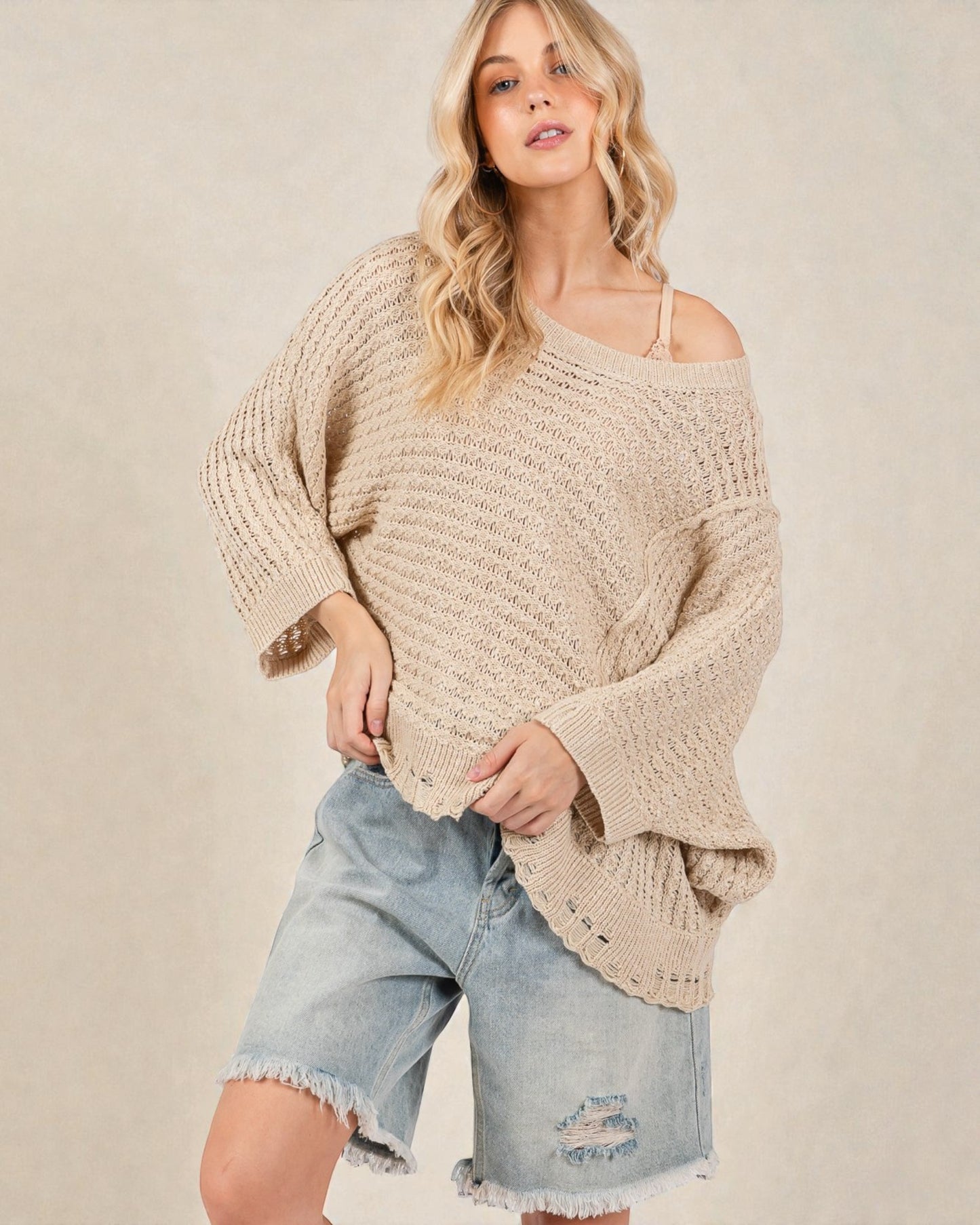 Woman wearing a beige chunky knit sweater and denim shorts on a plain background