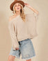 Woman wearing a beige chunky knit sweater and denim shorts against a beige background