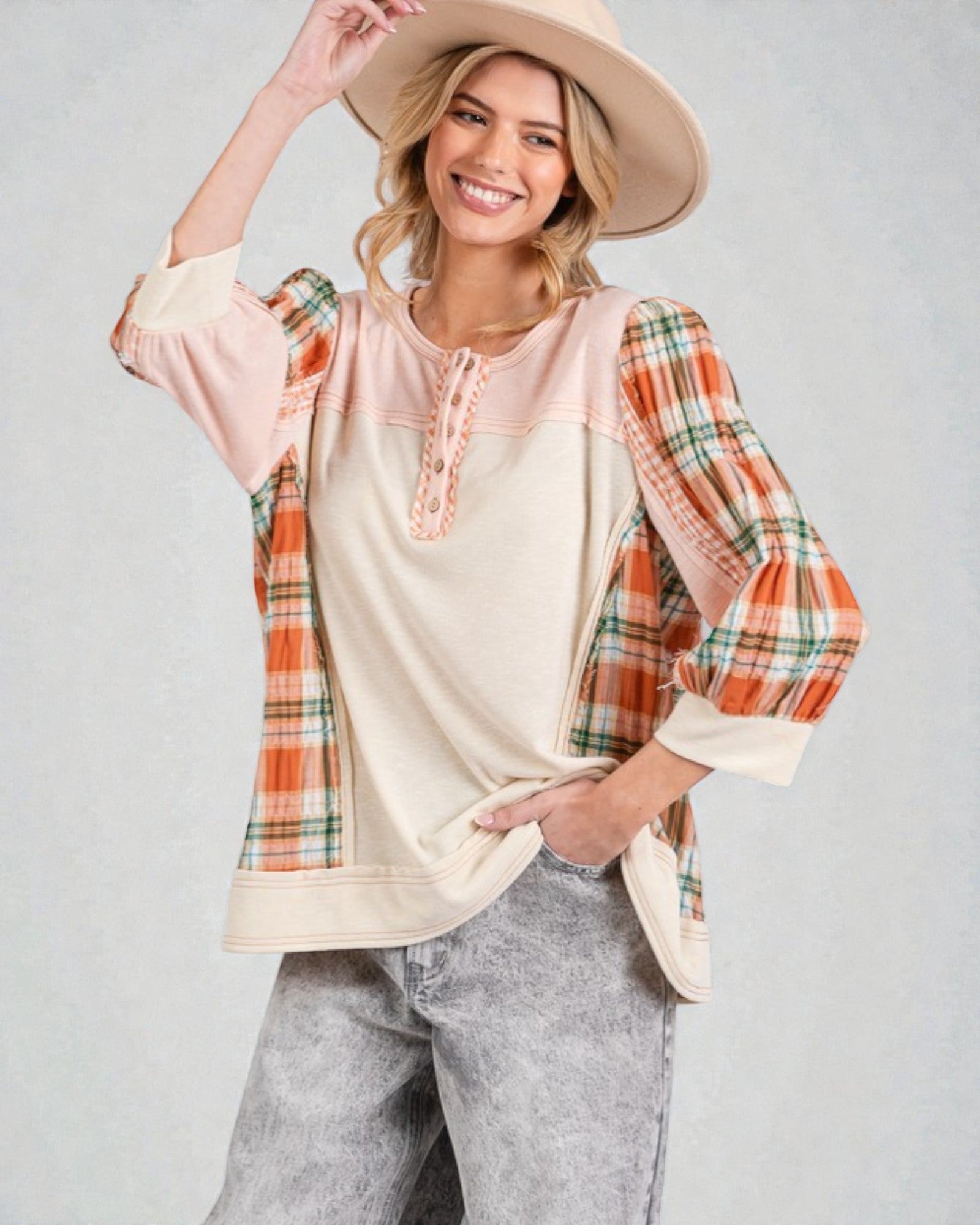 Woman wearing a plaid shirt over a beige top with gray pants on a plain background
