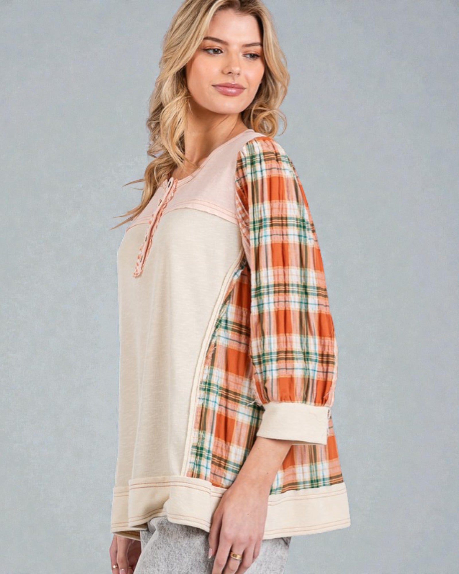 Woman wearing a plaid shirt over a beige top on a gray background
